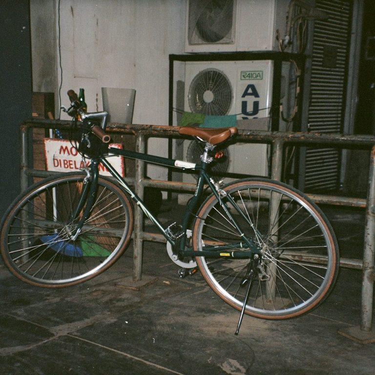 Schwarzes Fahrrad mit braunem Sattel, neben einer Wand mit Klimaanlage.