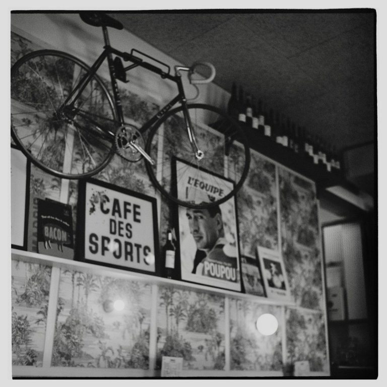 Wanddekoration mit einem Fahrrad und mehreren gerahmten Plakaten in Schwarz-Weiß.